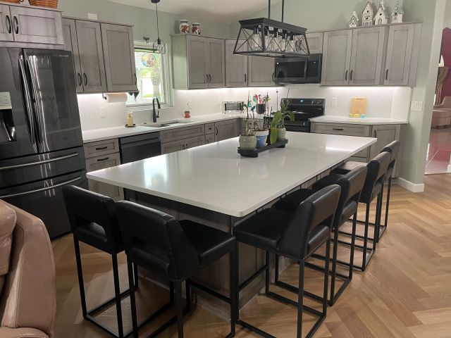 This stunning kitchen showcases Peppercorn-stained semi-custom cabinetry, quartz countertops with a matching full-height backsplash, and sleek matte black fixtures and hardware.