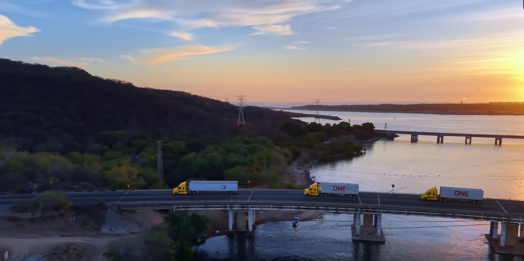 Camión rojo circulando por una carretera de montaña al atardecer, con paisajes montañosos al fondo.