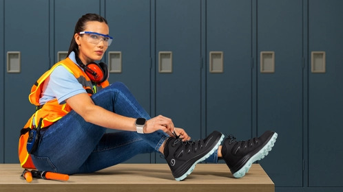 Bota de trabajo negra en un entorno industrial, con persona usando jeans.