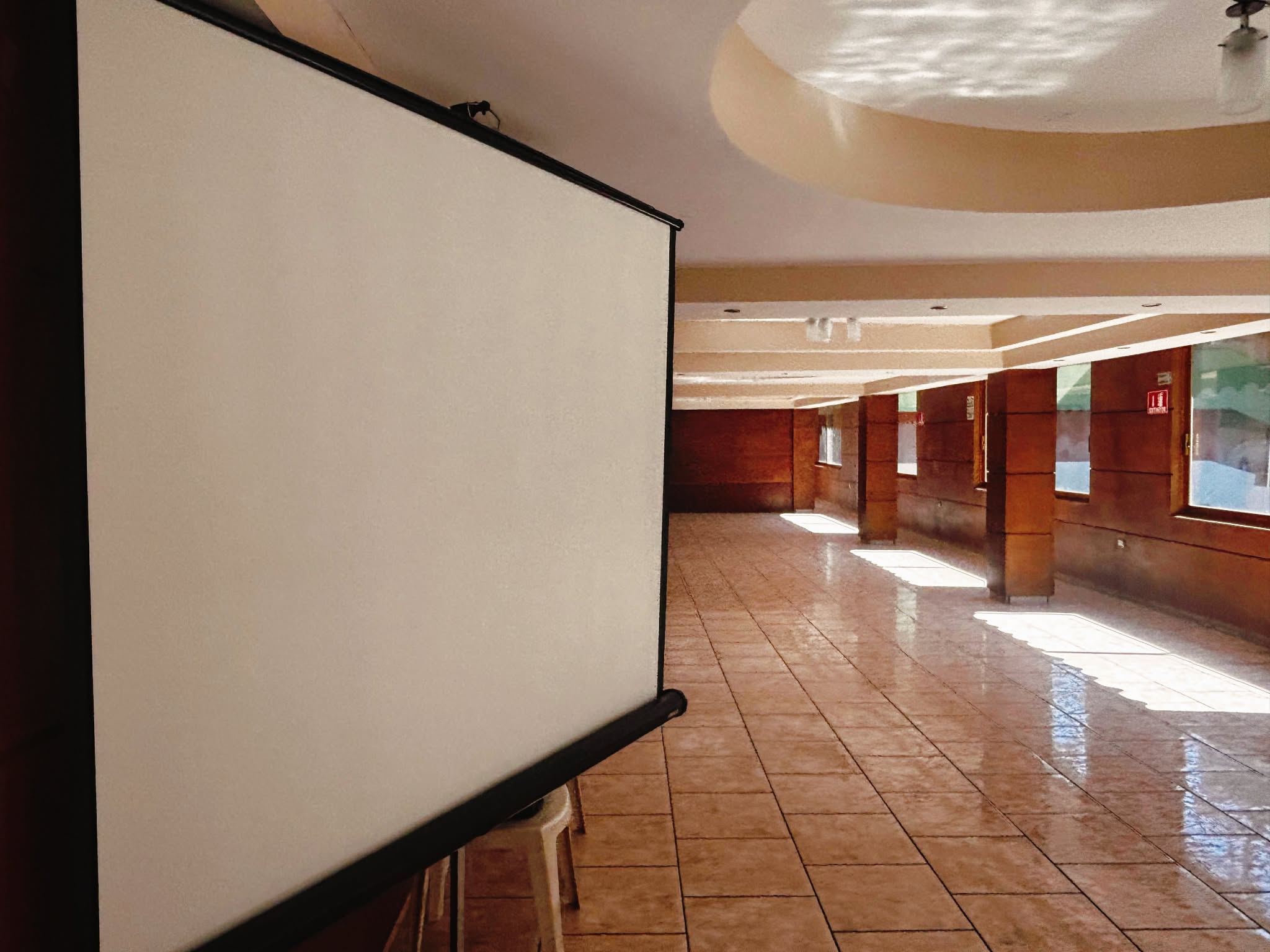 Sala de estar moderna con sofá gris, cojines naranjas, grandes ventanales, plantas colgantes y balcón con vistas al bosque.
