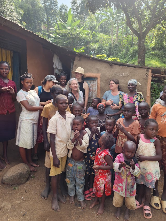Group of people, including children and adults, gathered outside a rustic building in a lush rural setting.