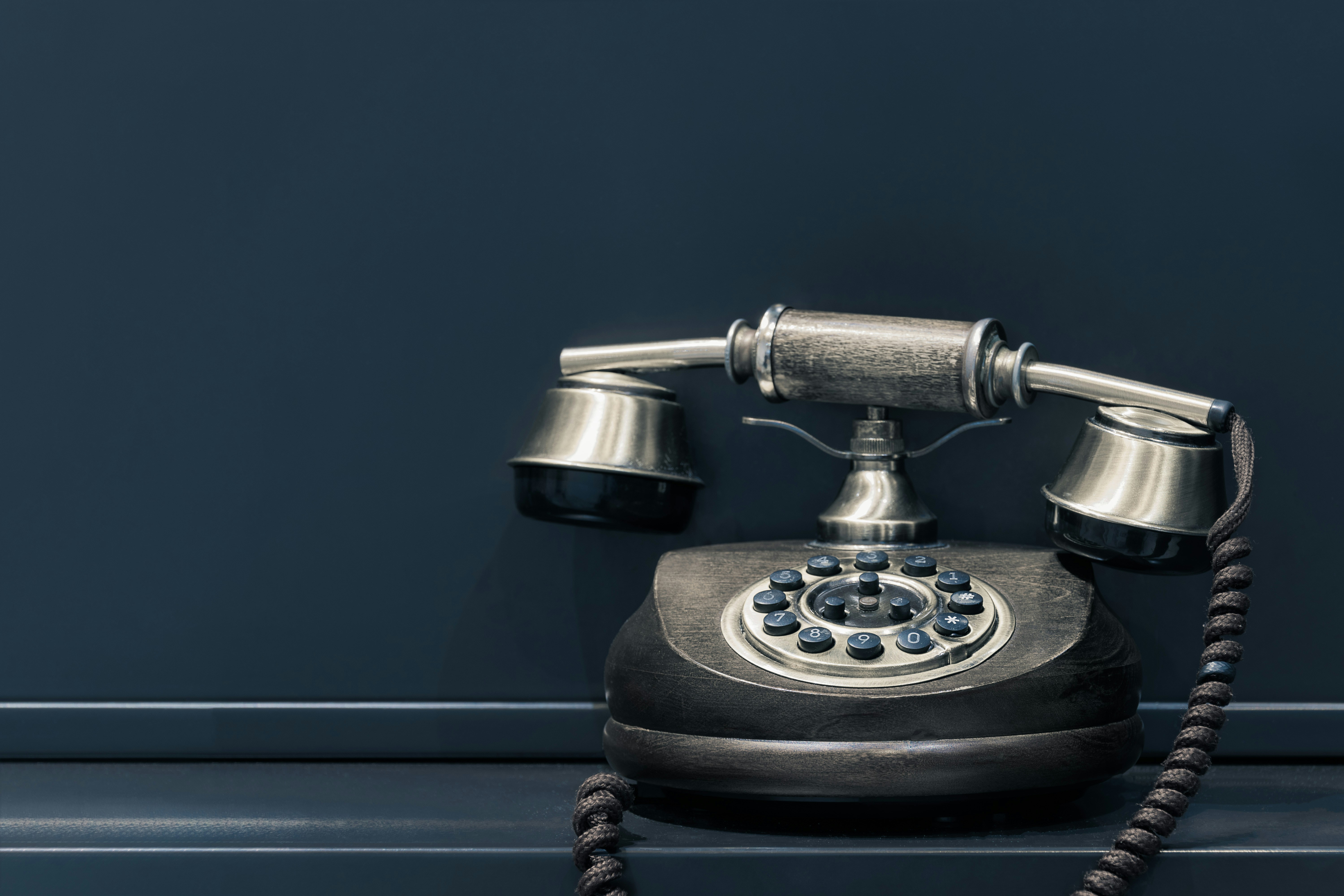 Vintage rotary telephone with metal and wood finish on a dark background.