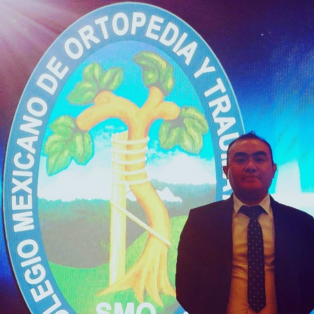 Hombre de traje posando frente a un emblema del Colegio Mexicano de Ortopedia y Traumatología con un diseño de árbol y muleta.