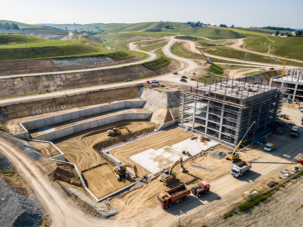 Vista aérea de obra en construcción con maquinaria pesada, edificio en estructura y carreteras en desarrollo