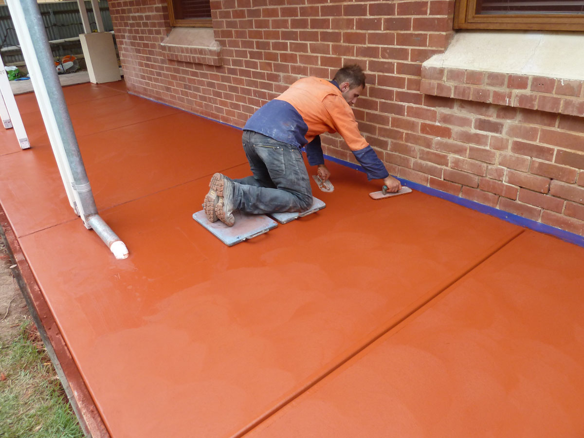 Worker smoothing freshly sealed orange concrete patio beside a brick house Worker smoothing freshly sealed orange concrete patio beside a brick house