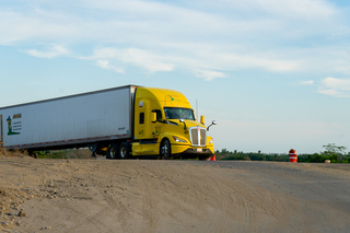 Camión blanco de carga circulando por carretera con palmeras y edificio moderno a un lado.