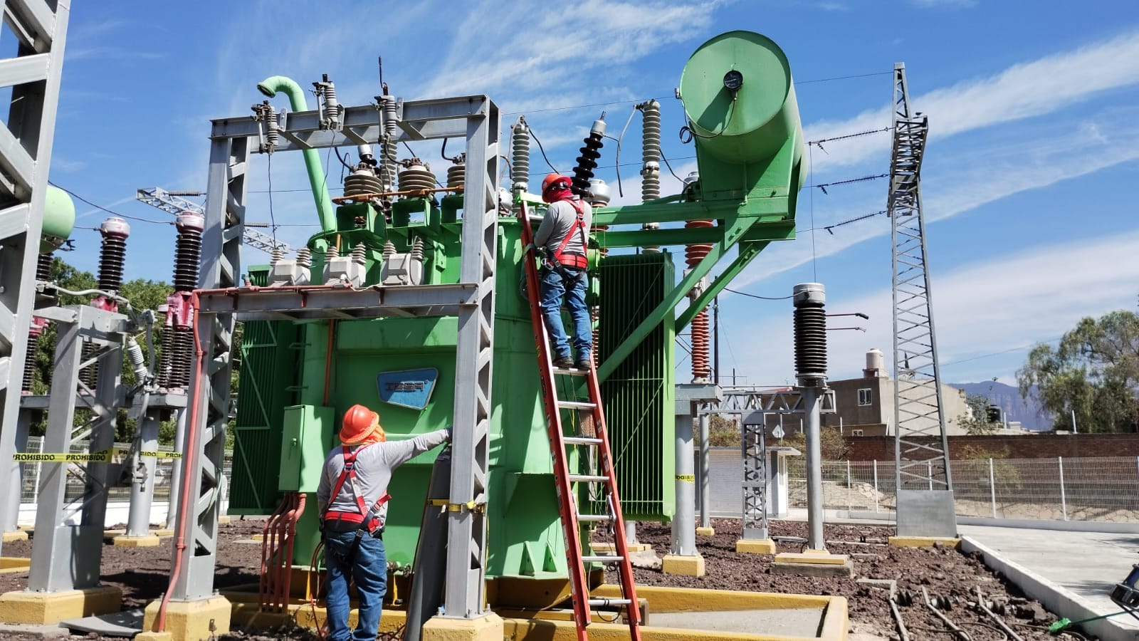 Ingeniero sonriente con casco amarillo cruzado de brazos en una fábrica moderna.