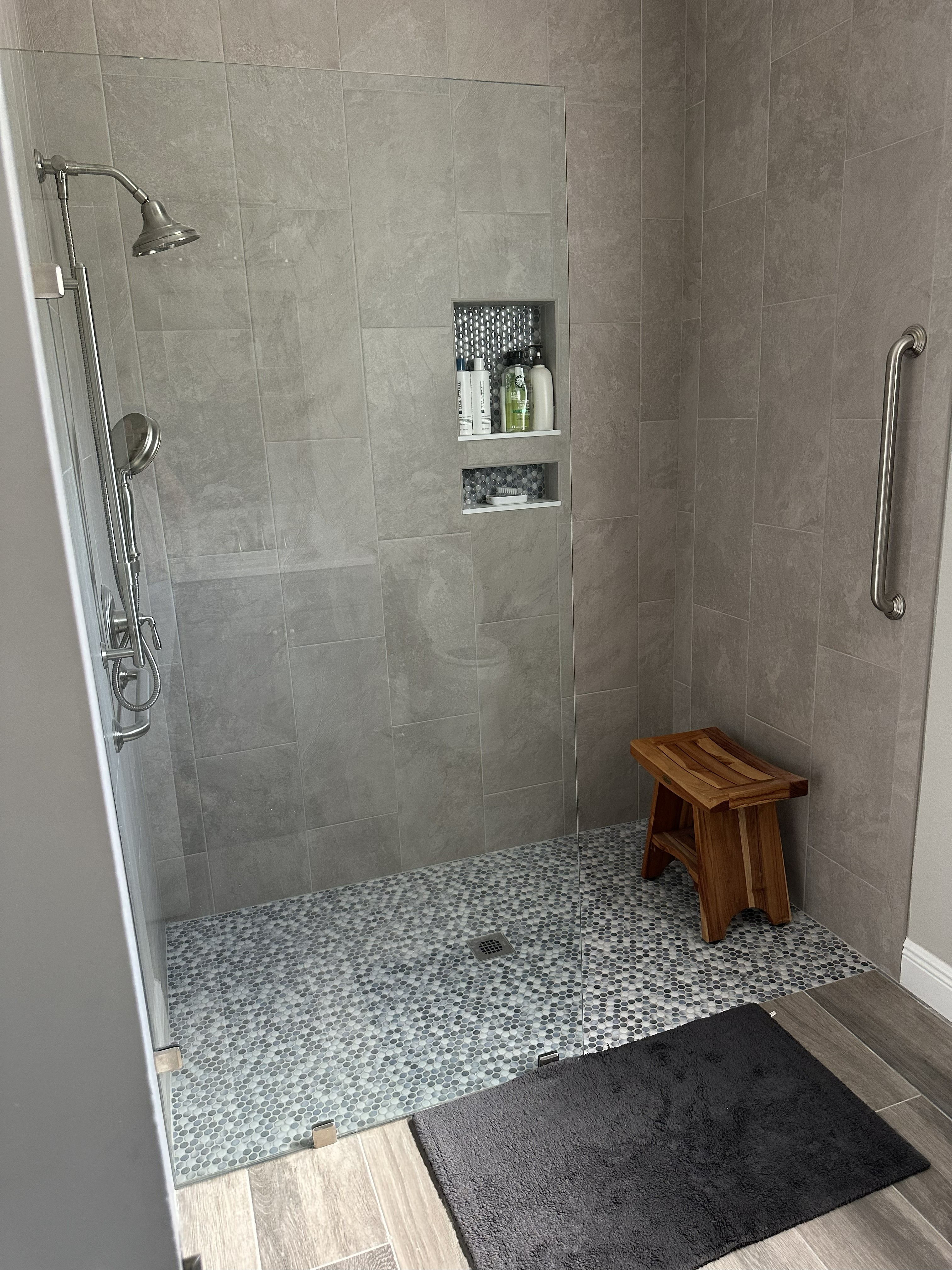 Spacious walk-in shower featuring two niches, 12x24 matte gray wall tile with matching bullnose, 
glossy penny rounds on the shower floor and in the niches, and a 3/8" heavy glass panel.