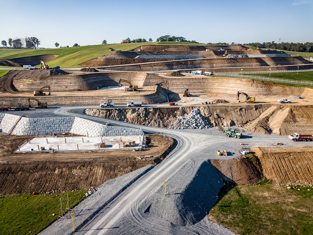 Vista aérea de obra de construcción vial con excavadoras, camiones y caminos de grava en terreno excavado