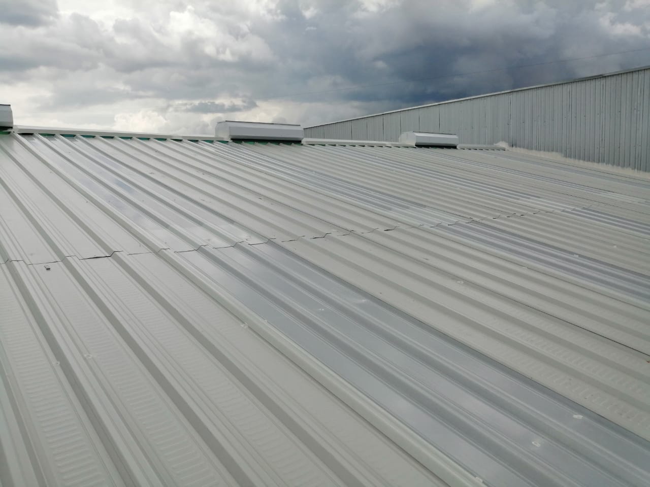 Sistema de ventilación instalado en el techo de un edificio industrial, con cielo nublado de fondo.
