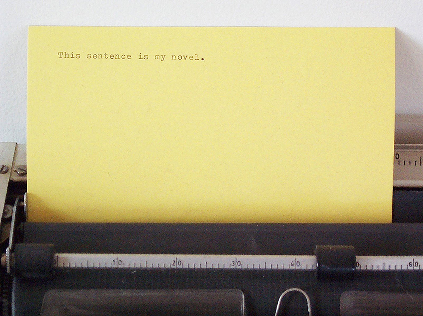 On a yellow card inserted in a typewriter is typed, “This sentence is my novel.”