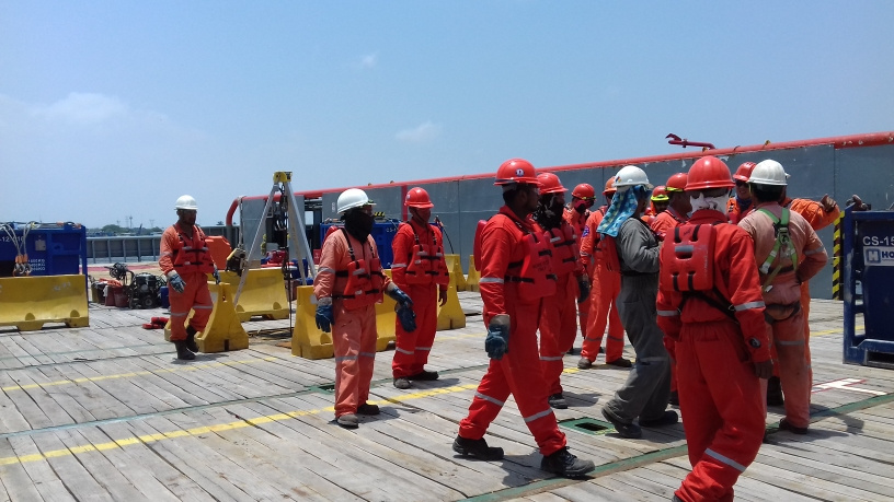 Trabajadores en una plataforma petrolera marina usando trajes de seguridad y cascos blancos.