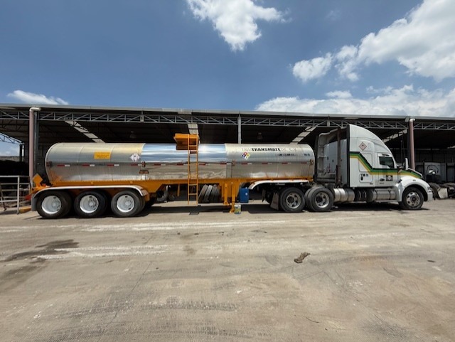Camión cisterna estacionado en un almacén bajo un cielo azul con nubes.