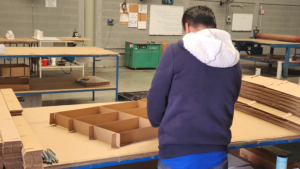 Oficina moderna con pantallas digitales mostrando información y código, personas trabajando y laptops sobre una mesa.