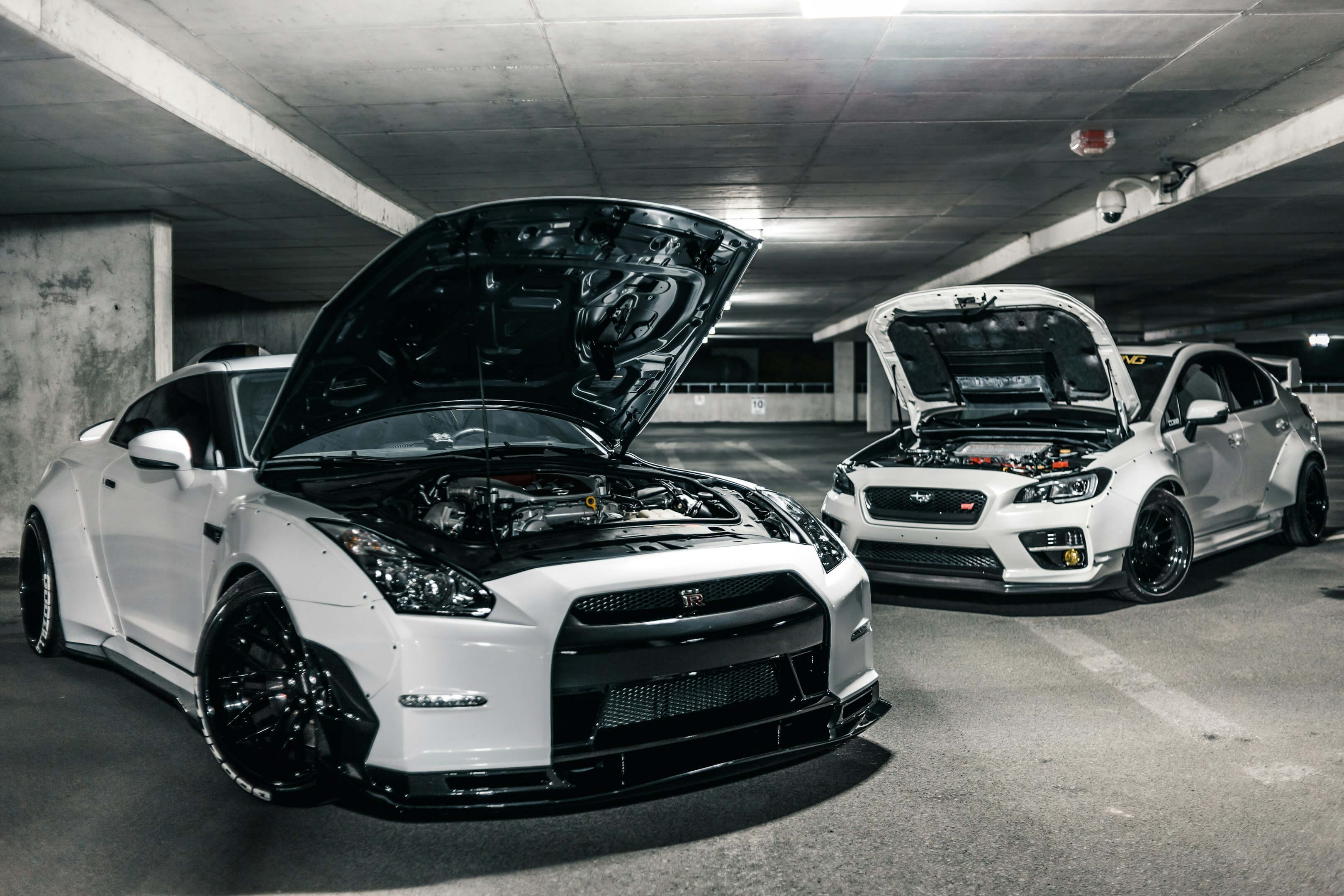 a white Nissan and Subaru with their hoods up
