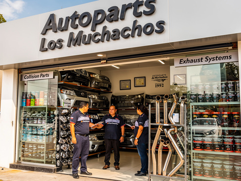Fachada de tienda AutoParts Los Muchachos con empleados y exhibición de repuestos y sistemas de escape
