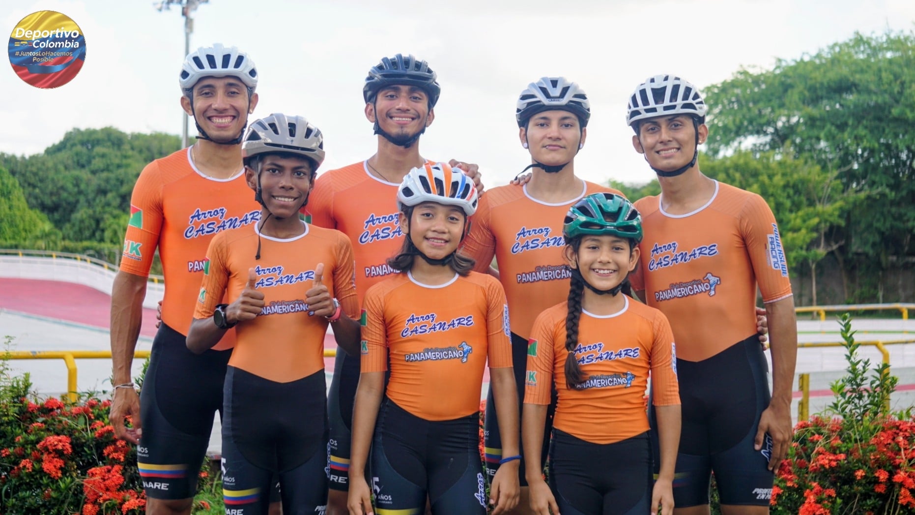 Equipo de ciclismo juvenil colombiano con uniformes naranjas y cascos en velódromo al aire libre