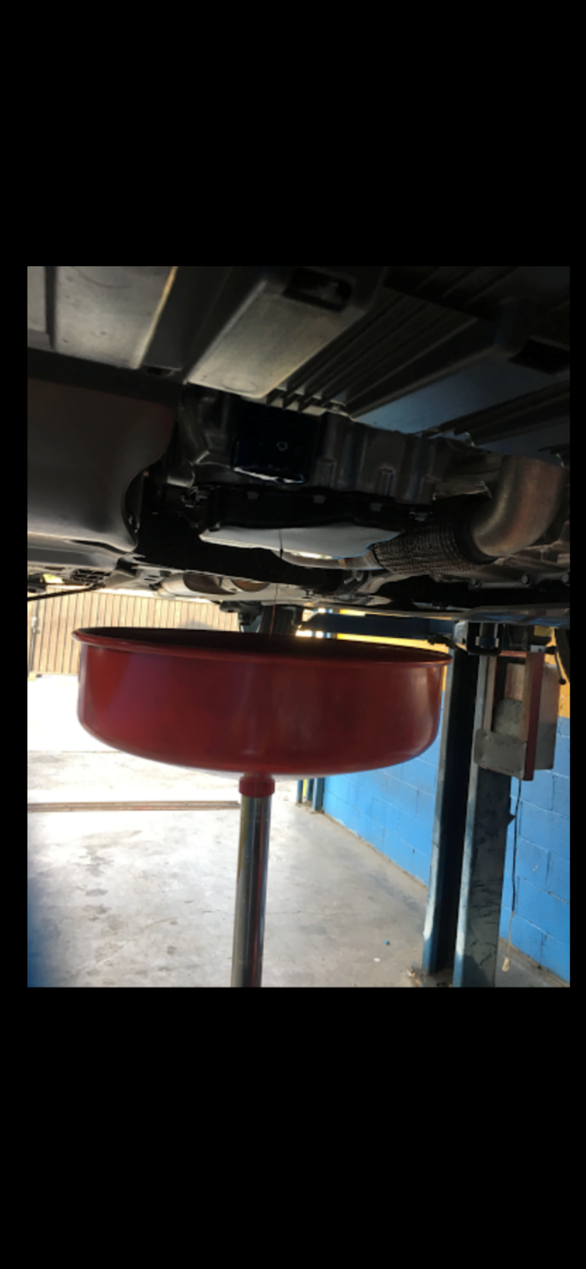 Car oil change with red drain pan under vehicle on garage lift