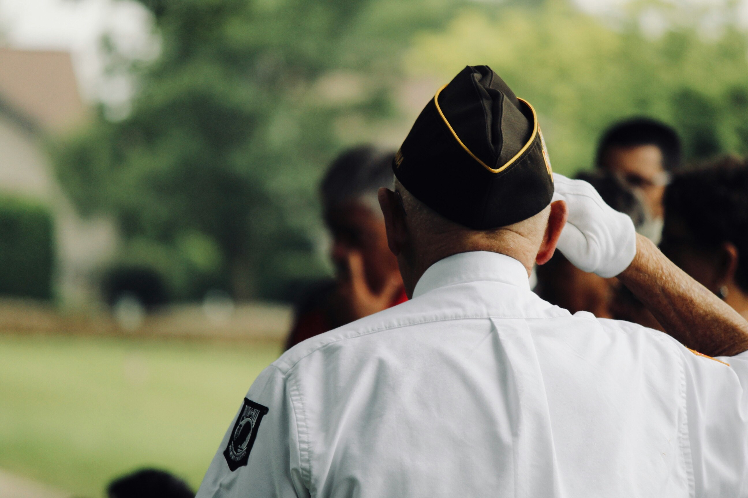 Veteran in uniform saluting at an outdoor event with blurred people in the background.