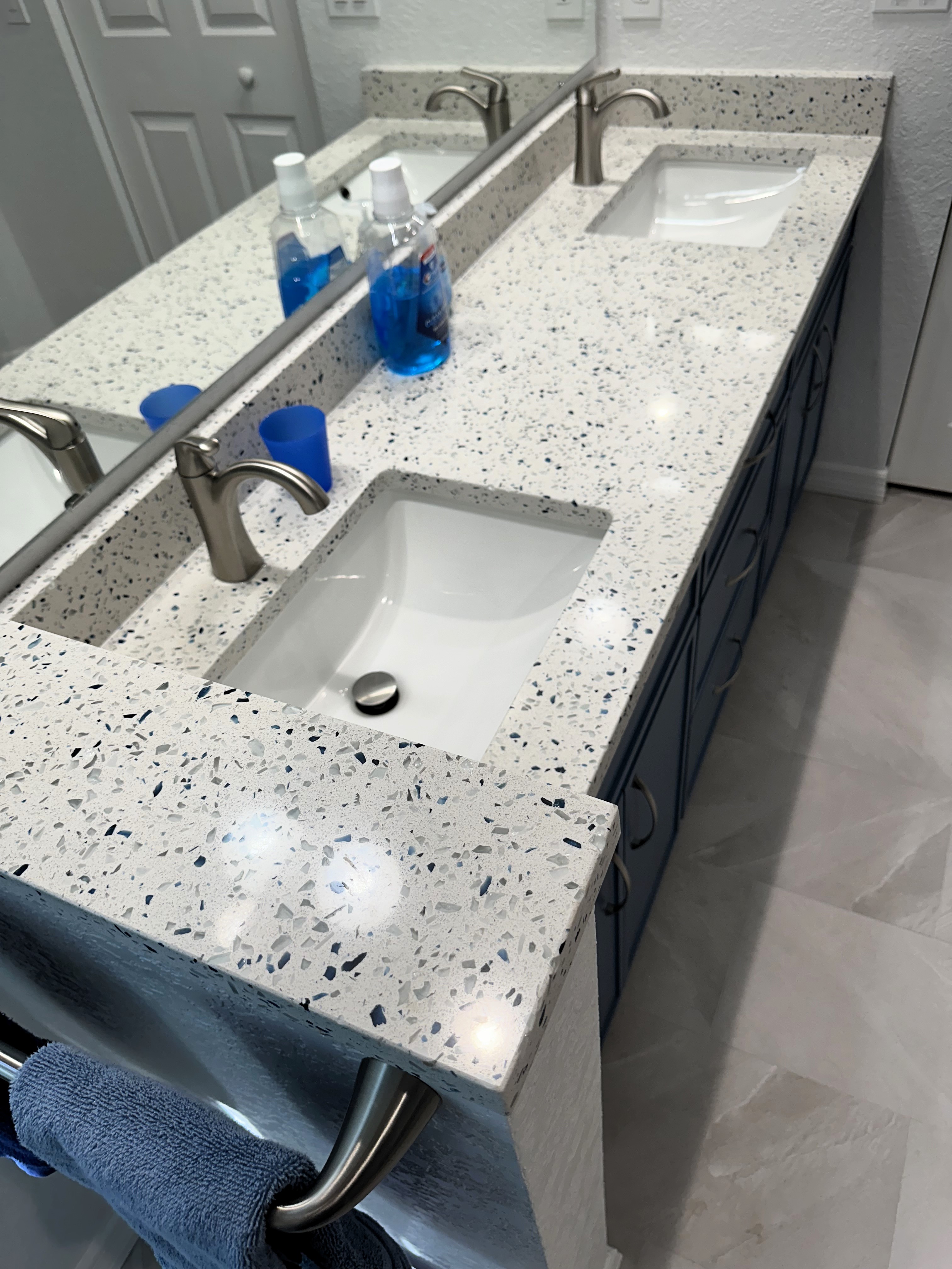 Stunning recycled glass quartz countertops, paired with sleek white rectangular undermount sinks and complemented by brushed nickel faucets, create a perfect balance of modern style and eco-conscious design.