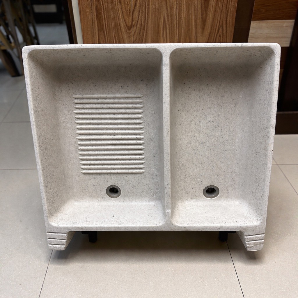 Baño moderno con bañera independiente, lavamanos sobre encimera, espejo circular, silla gris, plantas decorativas y ventana amplia.