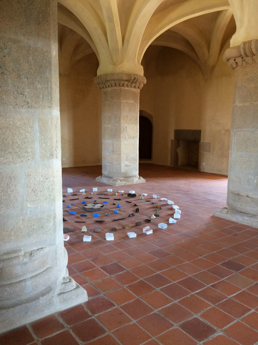 Rustic objects arranged in concentric circles on a tile floor in a castle-like space.