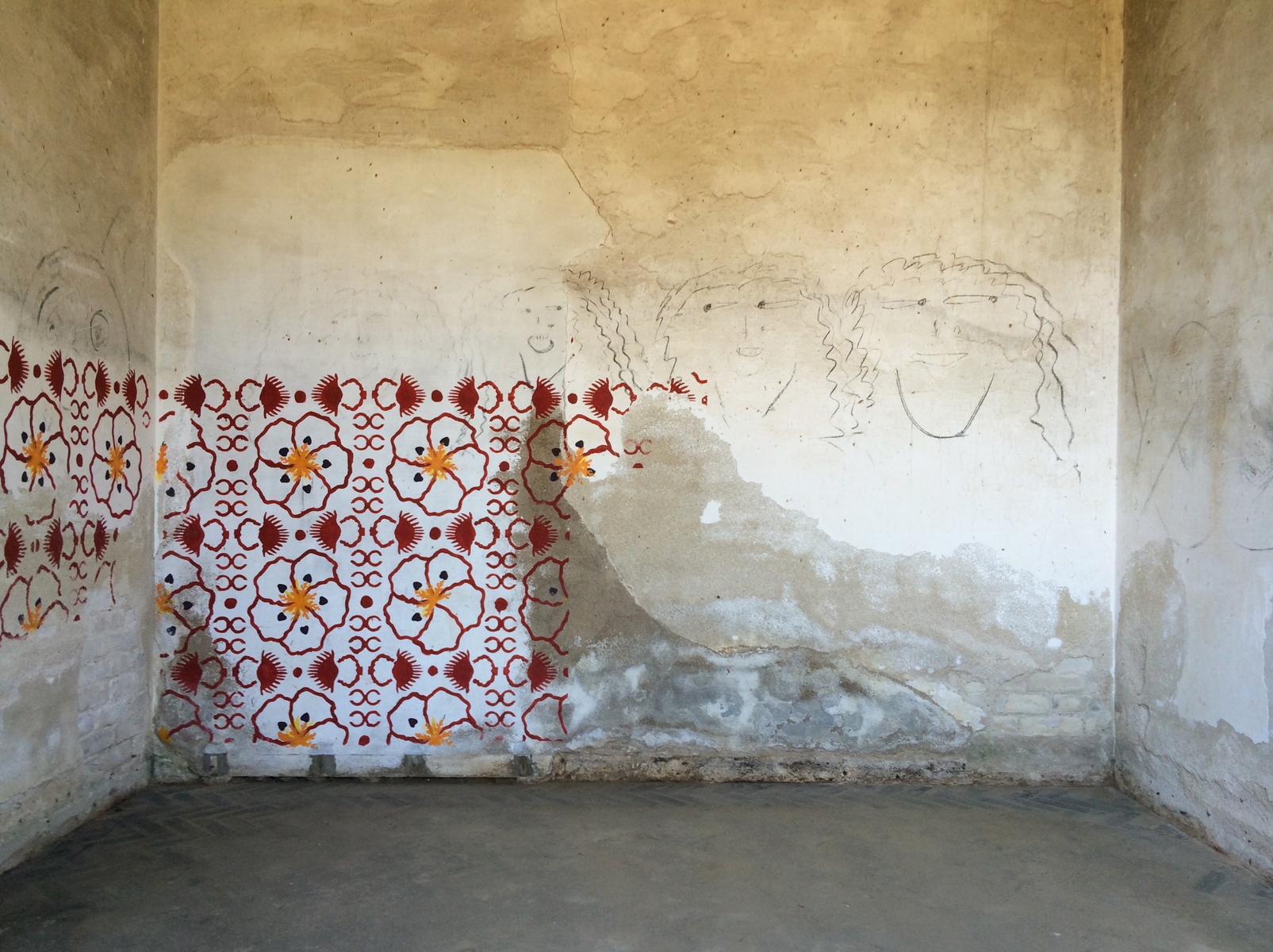 An empty rustic whitewashed room with a floral mural and charcoal-drawn faces.