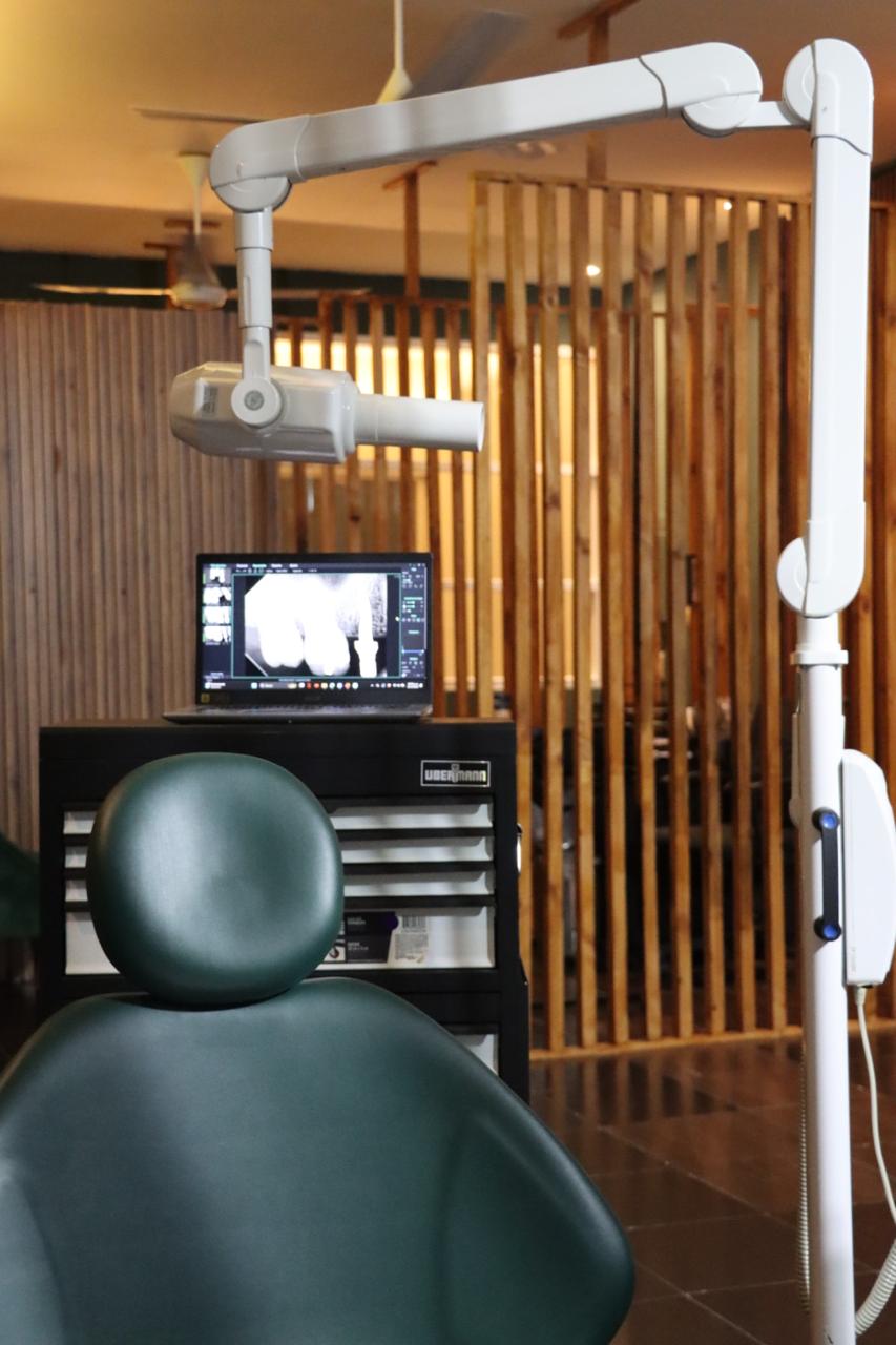 Consultorio dental con silla verde, lámpara dental y pantalla mostrando radiografía.