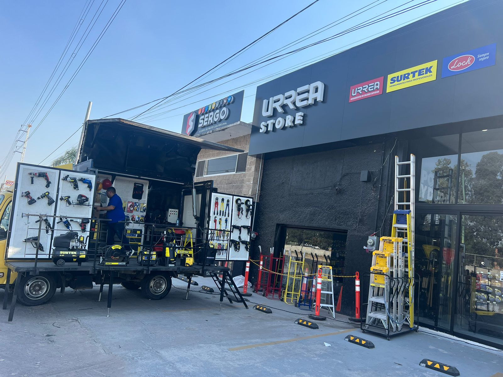 Camión de herramientas frente a Urrea Store, con equipo de construcción y escaleras expuestas.