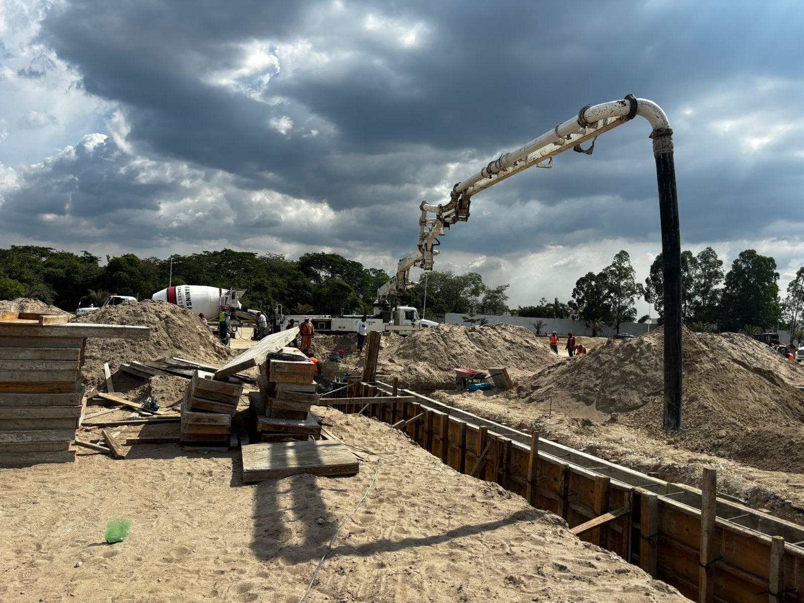 Obrero de construcción con casco junto a maquinaria pesada en obra ferroviaria urbana con grúas y rascacielos al fondo Obrero de construcción con casco junto a maquinaria pesada en obra ferroviaria urbana con grúas y rascacielos al fondo