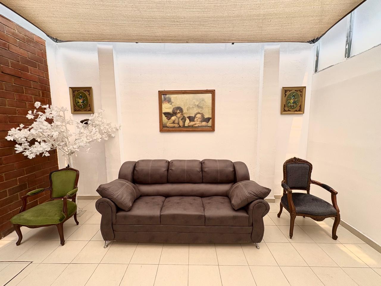 Pasillo moderno y luminoso con sillones amarillos y grises, junto a grandes ventanales y plantas decorativas.