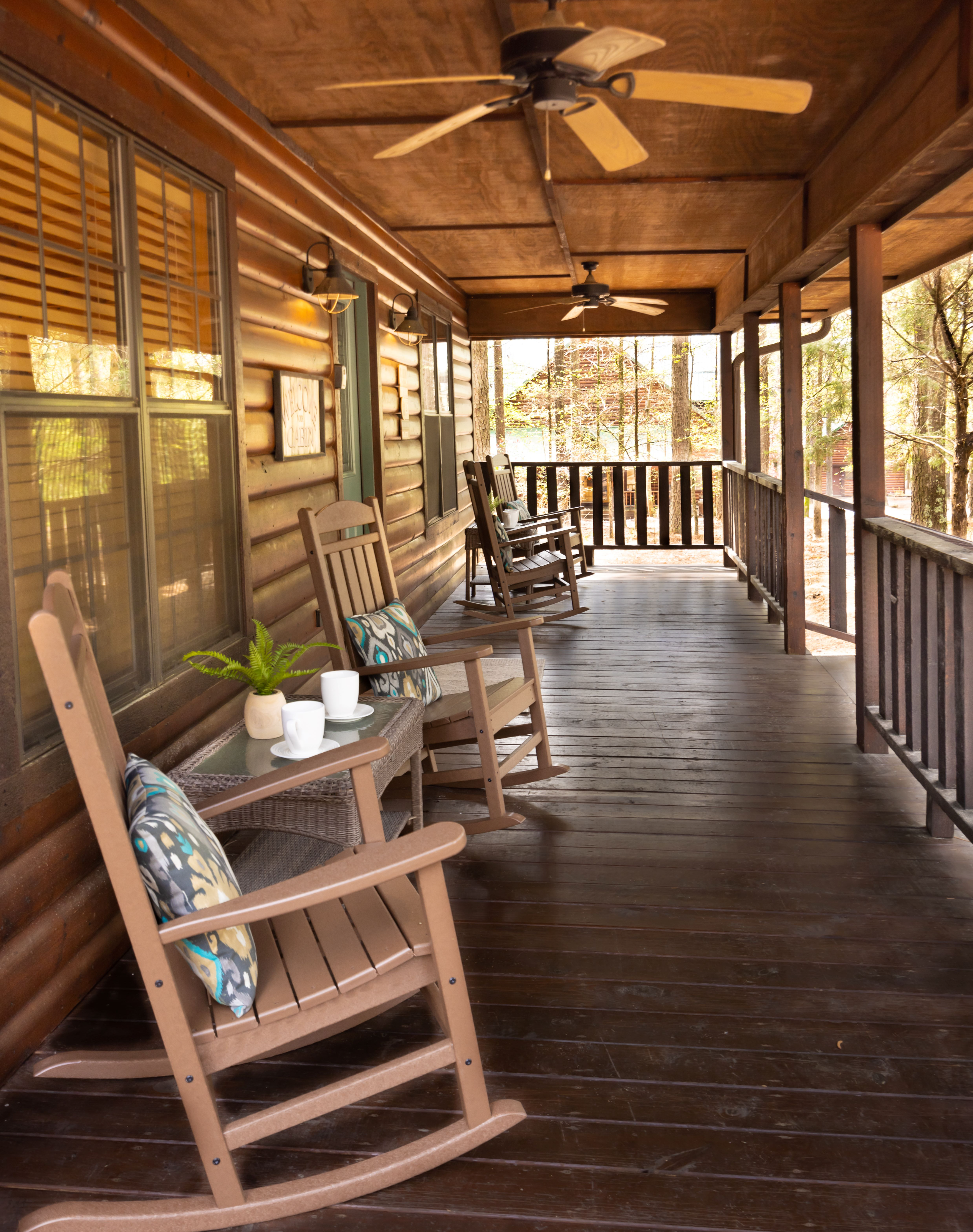 Charming rustic log cabin with a green roof surrounded by lush pine forest and natural landscaping.