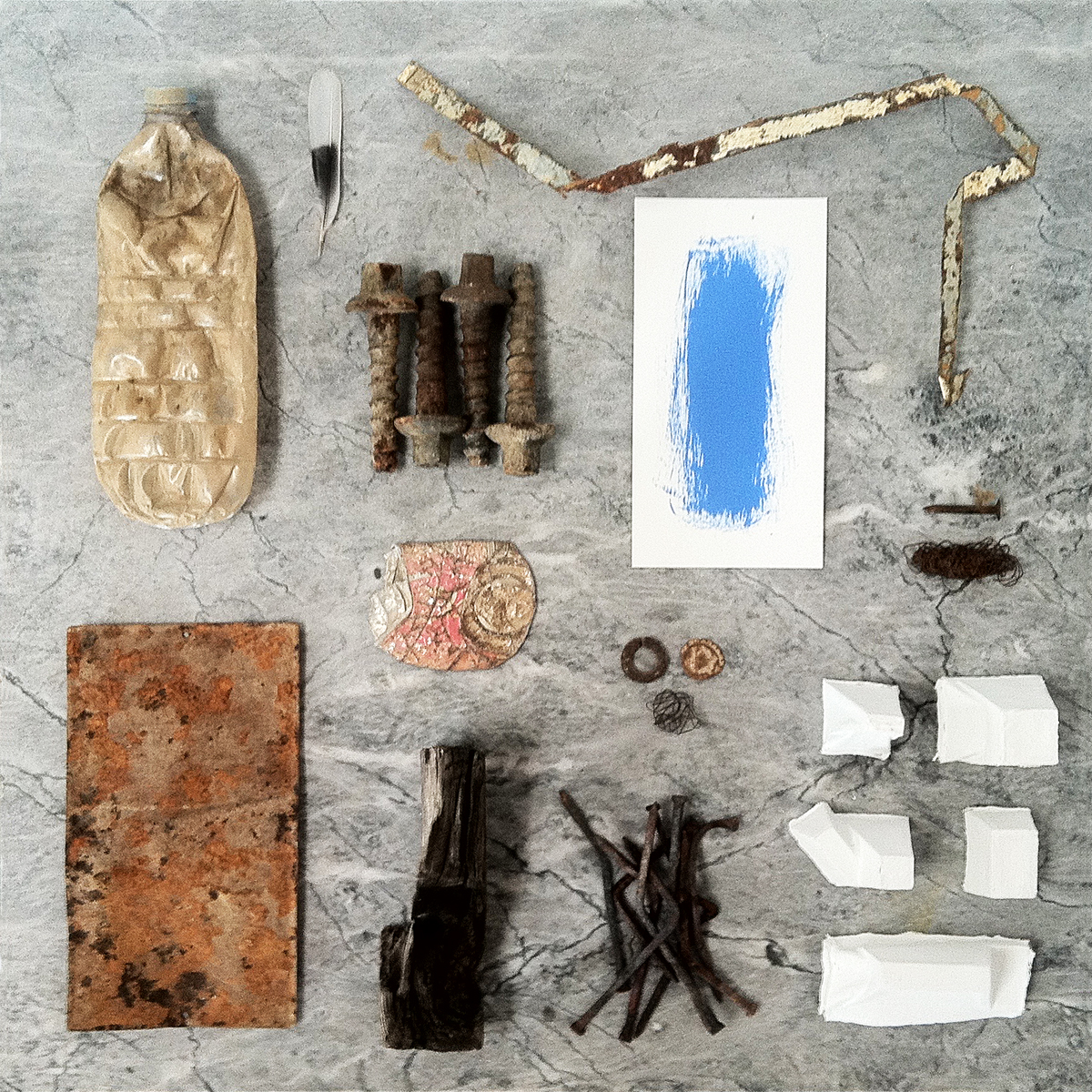 A feather, a blue painting on paper and other objects on a grey marble table.