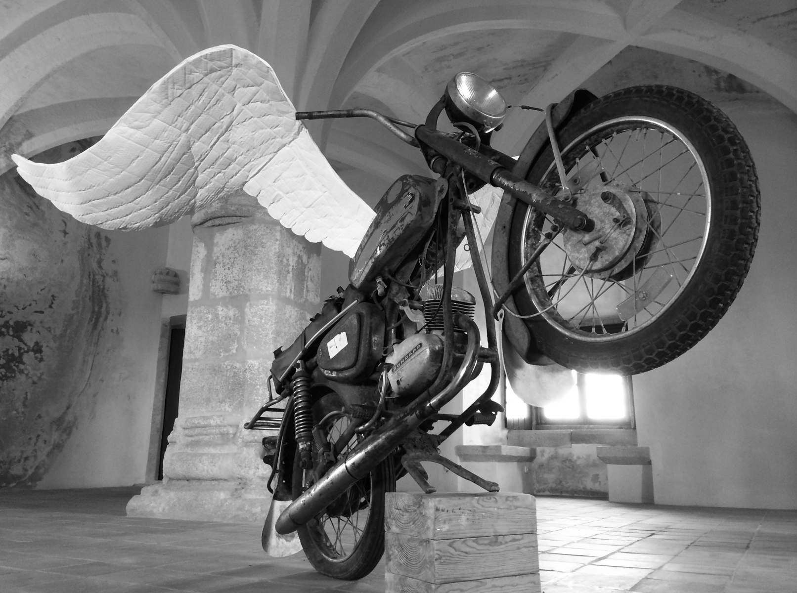 A rearing motorcycle with large white wings in a room with a vaulted ceiling.
