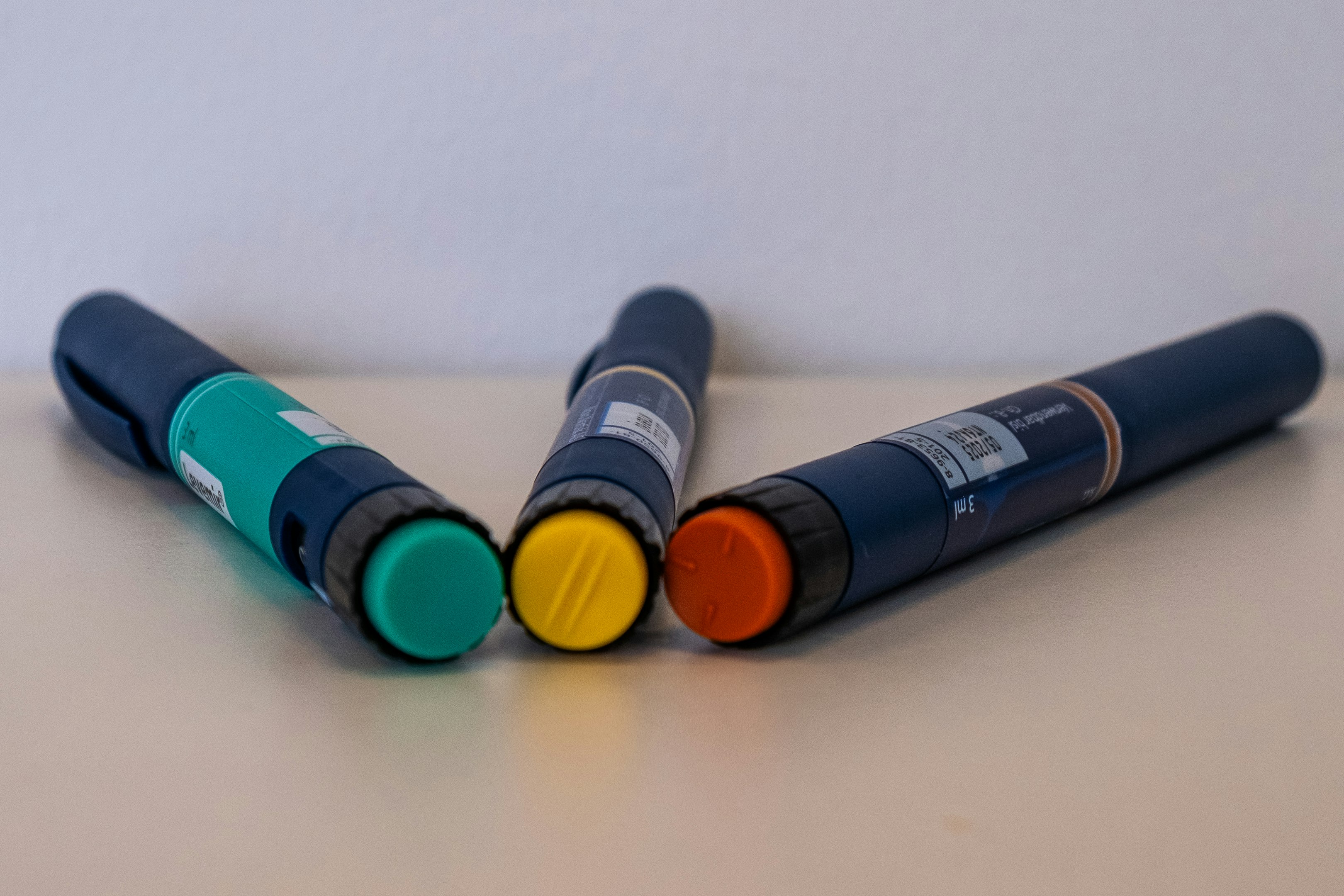 Three injection pens with colored caps on table.