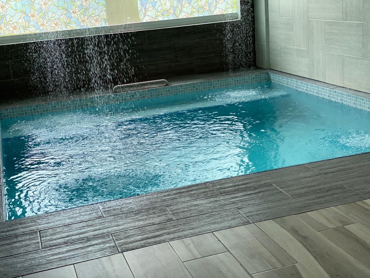 Piscina cubierta con diseño moderno, azulejos azul claro y cascada de agua en un entorno elegante.