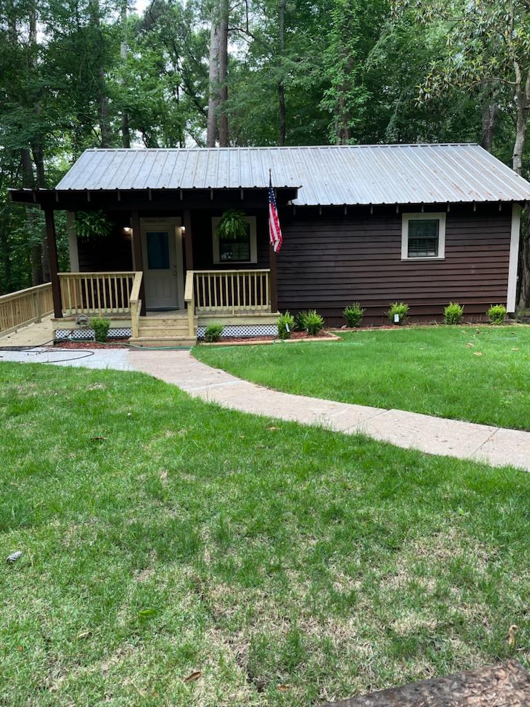 Rustic wooden cabin in a forest setting surrounded by tall trees and scattered leaves on the ground.