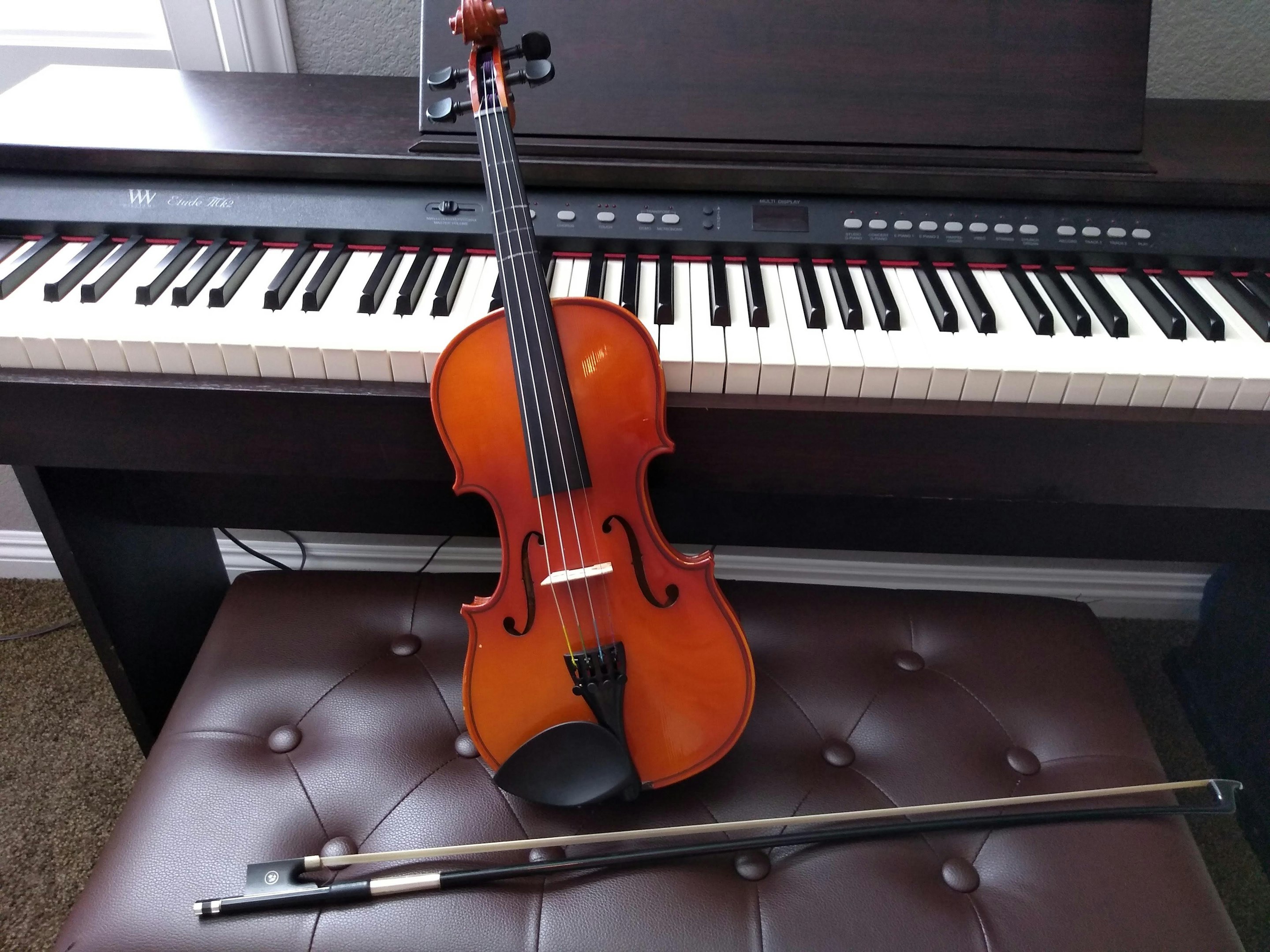 brown violin with brown violin bow beside white electronic keyboard