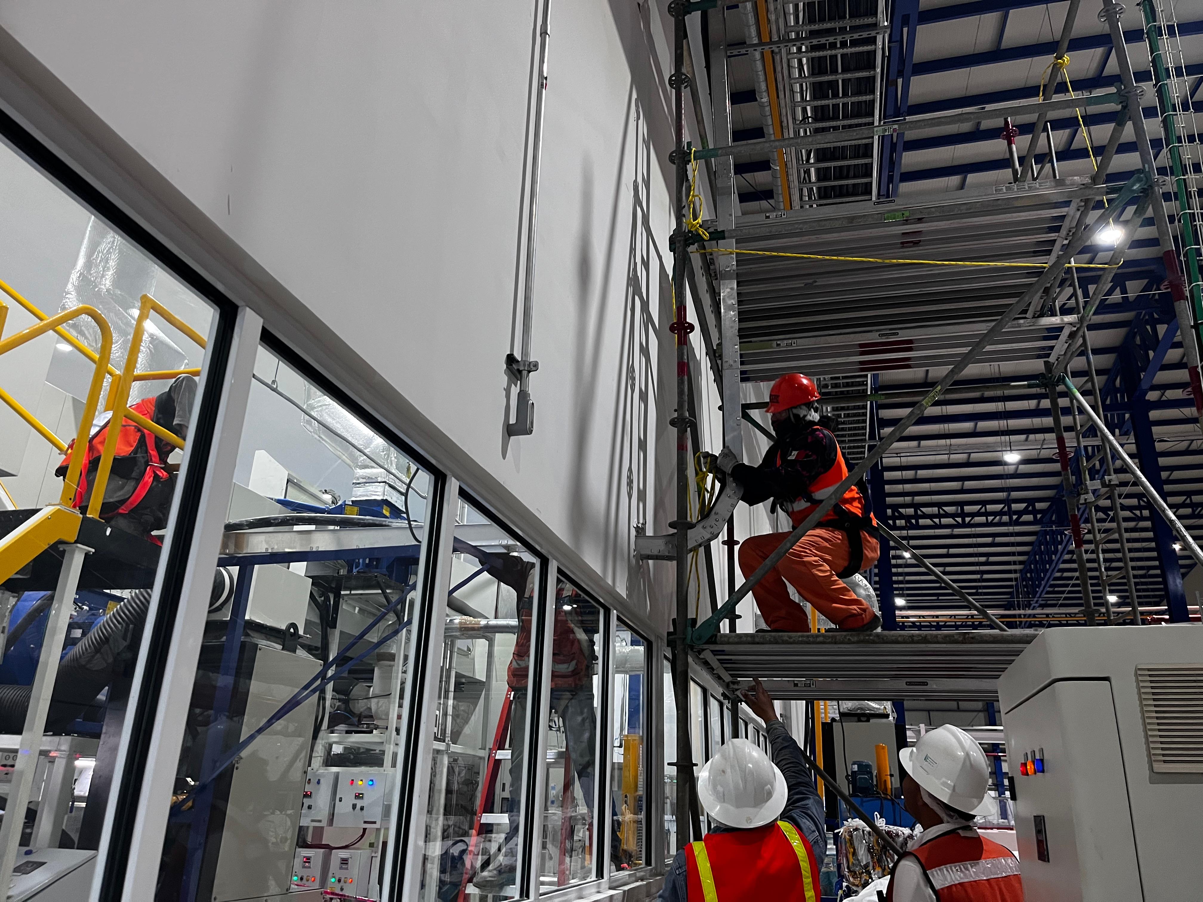Trabajadores en un sitio de construcción industrial, usando equipo de seguridad, realizando tareas de instalación en una estructura metálica.