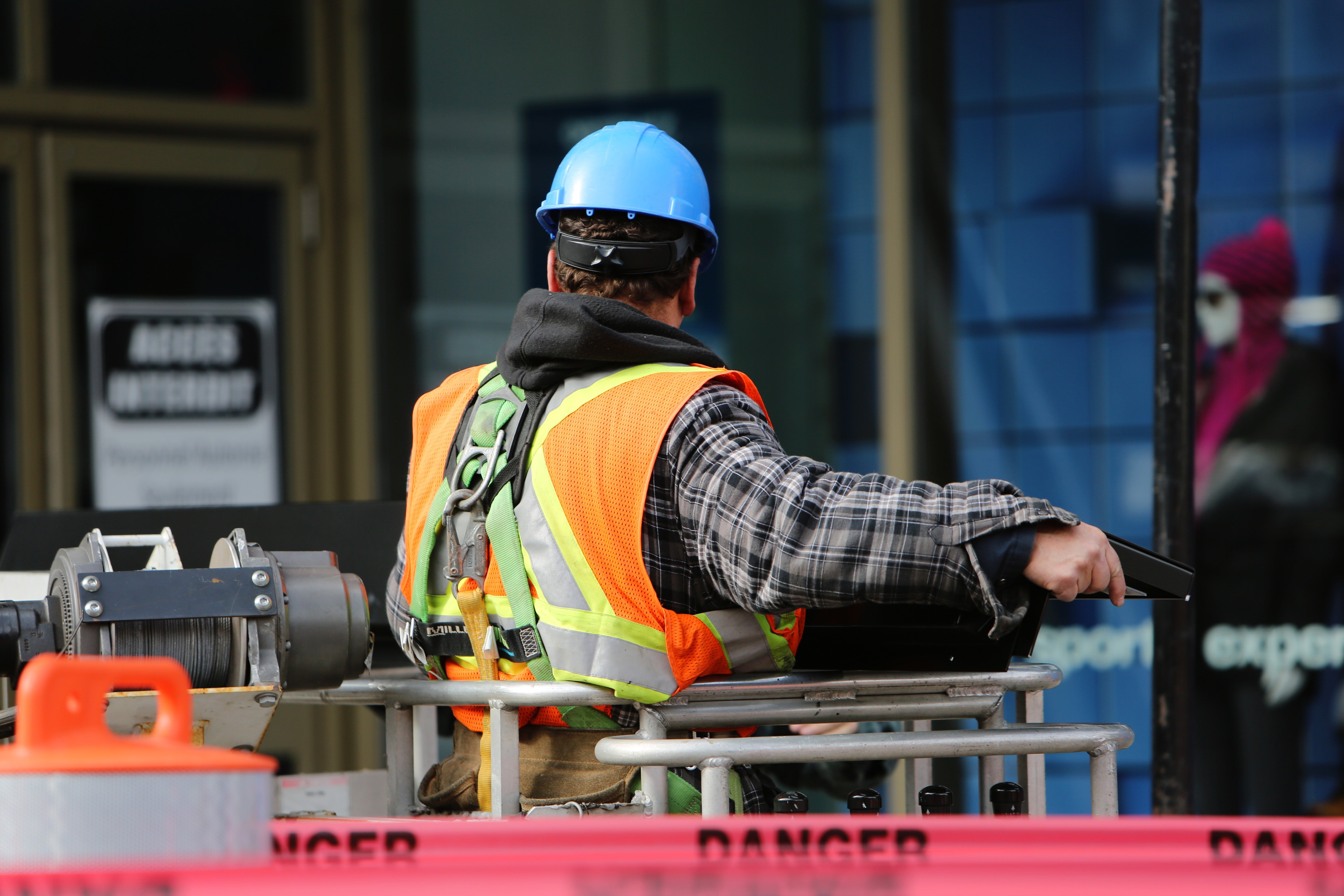 Trabajador de construcción con casco azul y chaleco reflectante usando arnés de seguridad en zona de obra