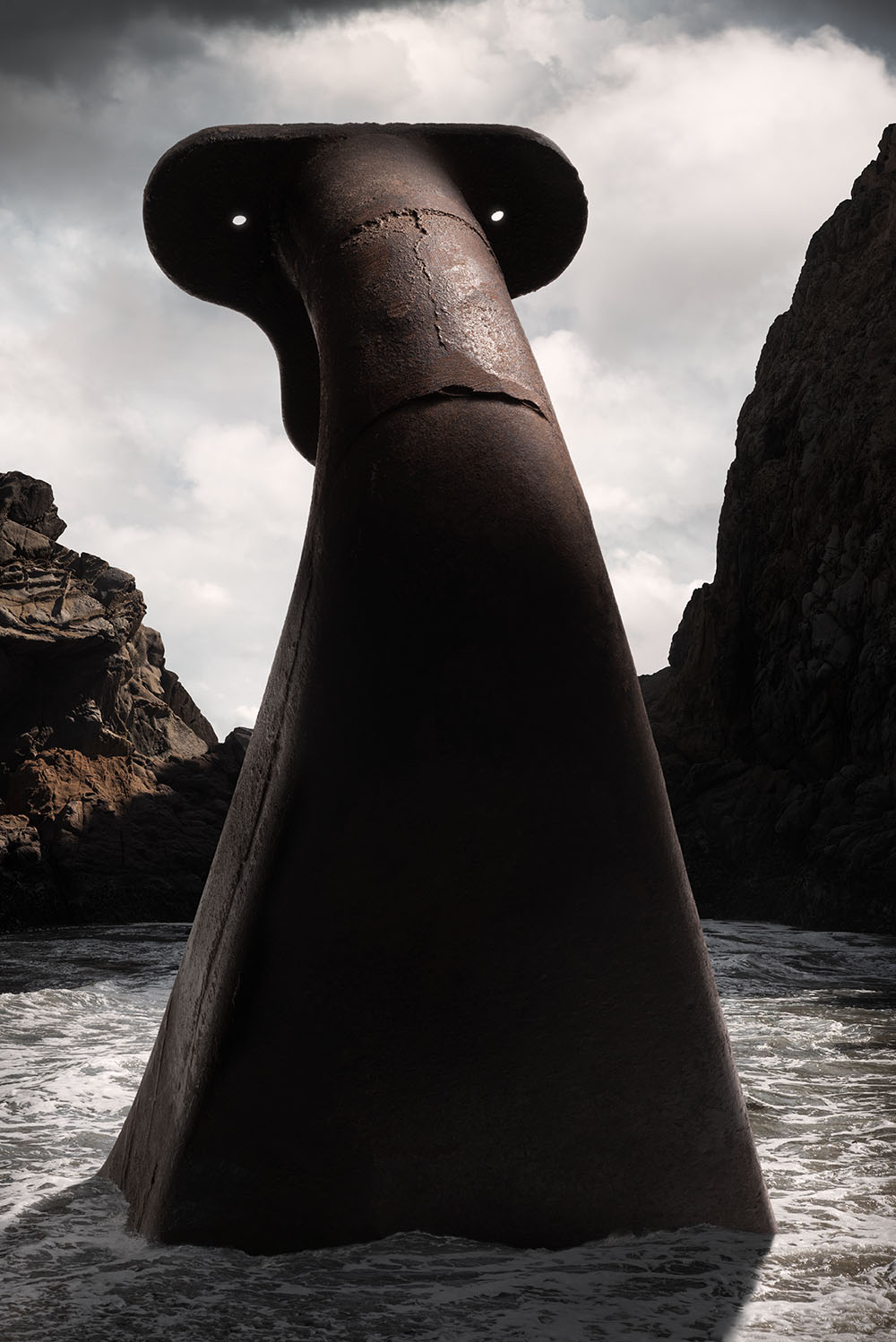 A menacing, giant metal structure rising from waters of ocean surf, dramatically lit against a stormy sky. 