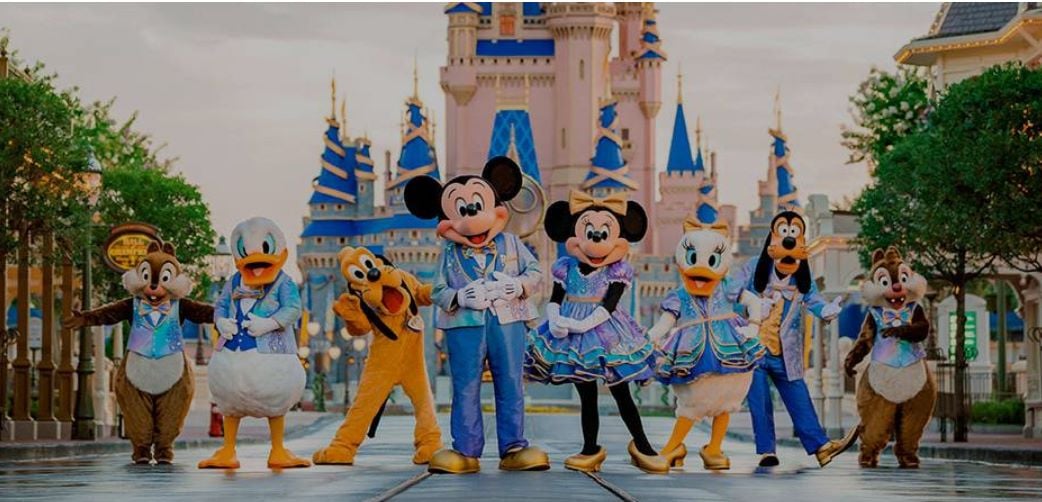 Personajes de dibujos animados en trajes brillantes frente a un castillo en un parque temático.