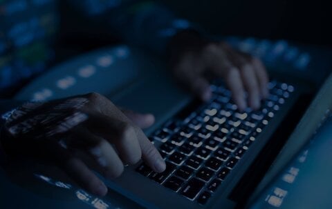 Persona tecleando en un teclado iluminado en un ambiente oscuro.