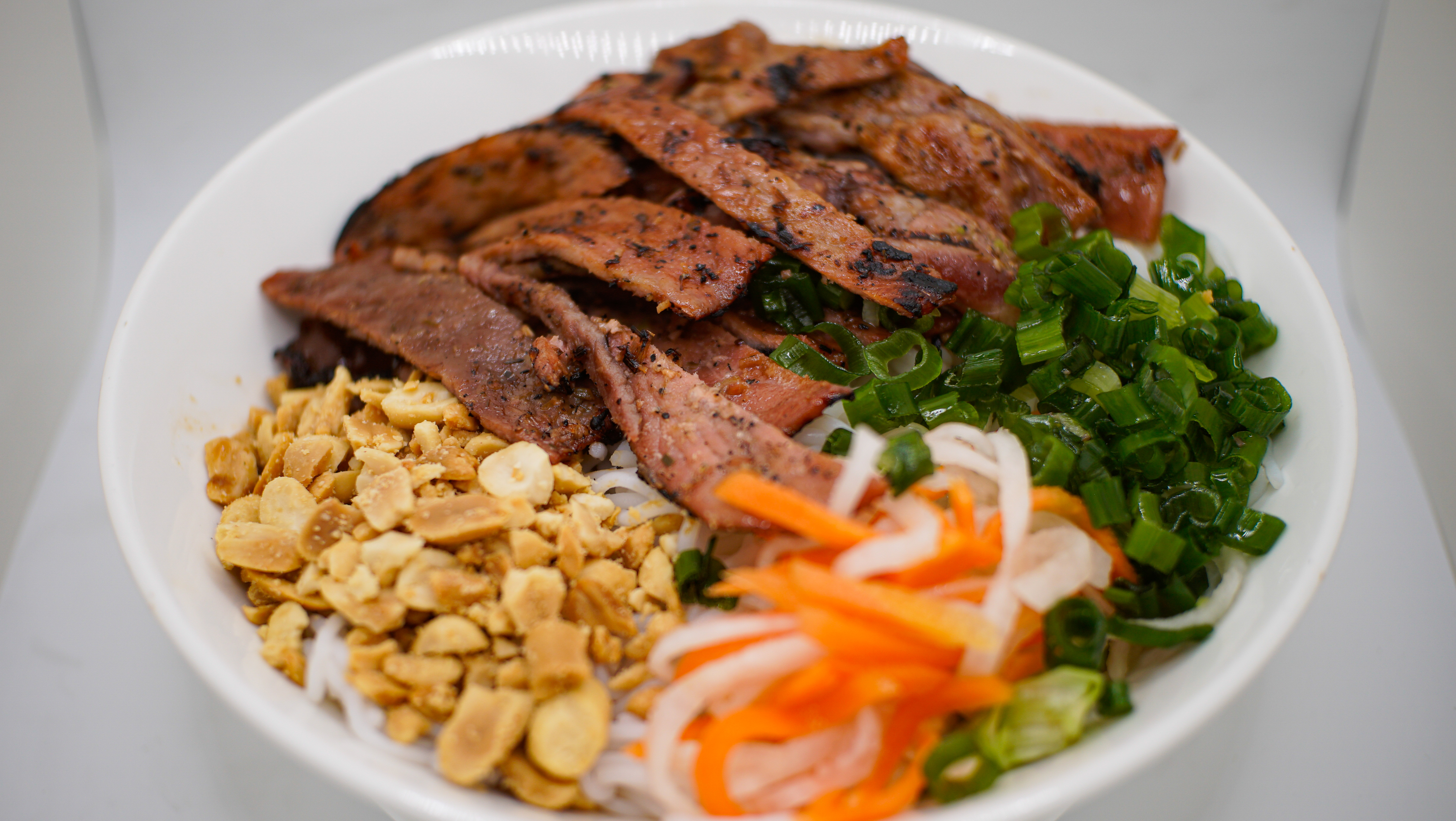 3B. BUN HEO NUONG (G)
Grilled Beef Vermicelli
Noodle Bowl
Topped W/ Crushed Peanuts, 
Pickled Carrots/Radish and
Oiled Green Onions
Served w/ Sweet Sour Fish Sauce