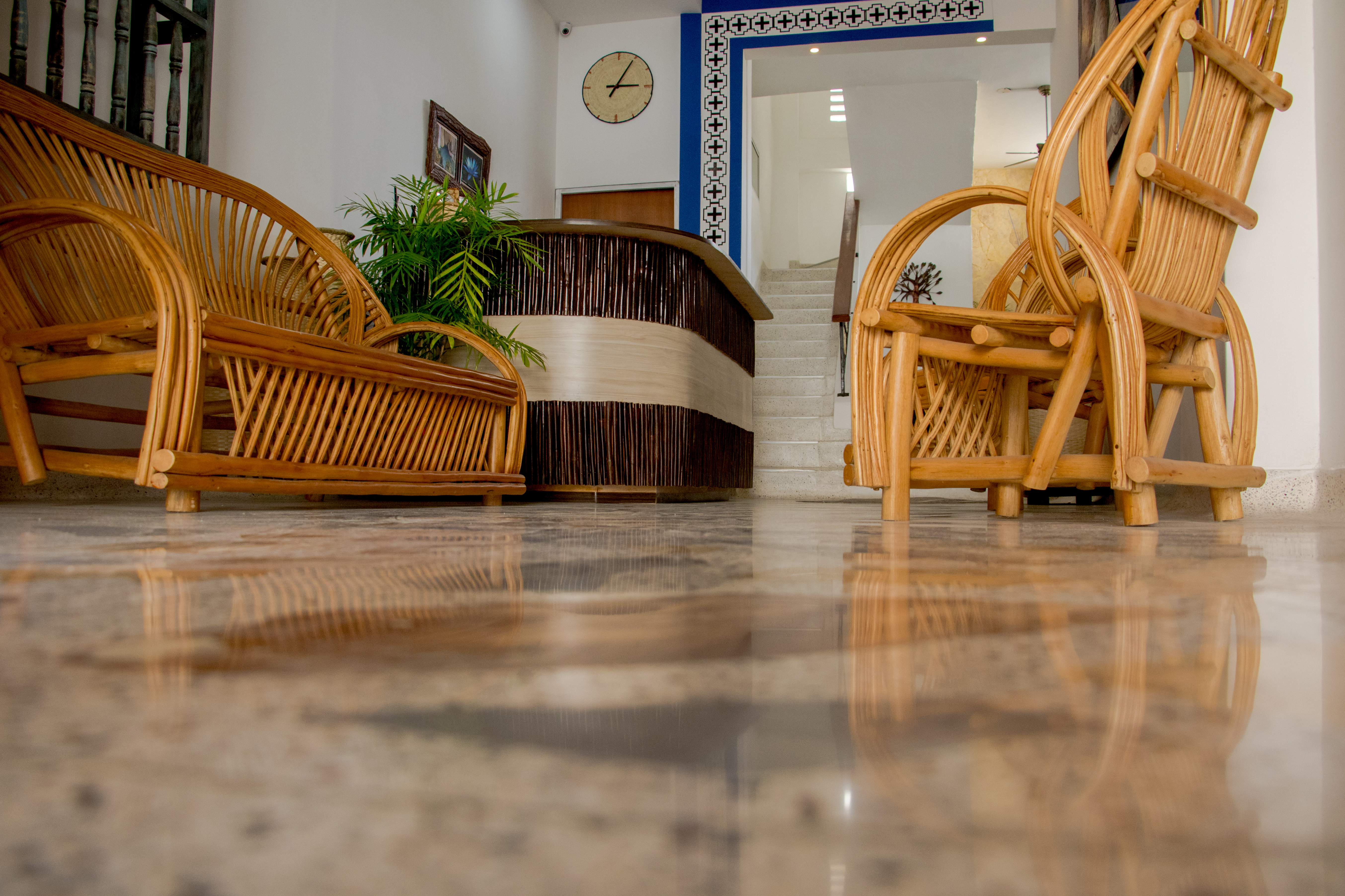 Mobiliario de mimbre en sala de espera con reloj en pared y escaleras al fondo.