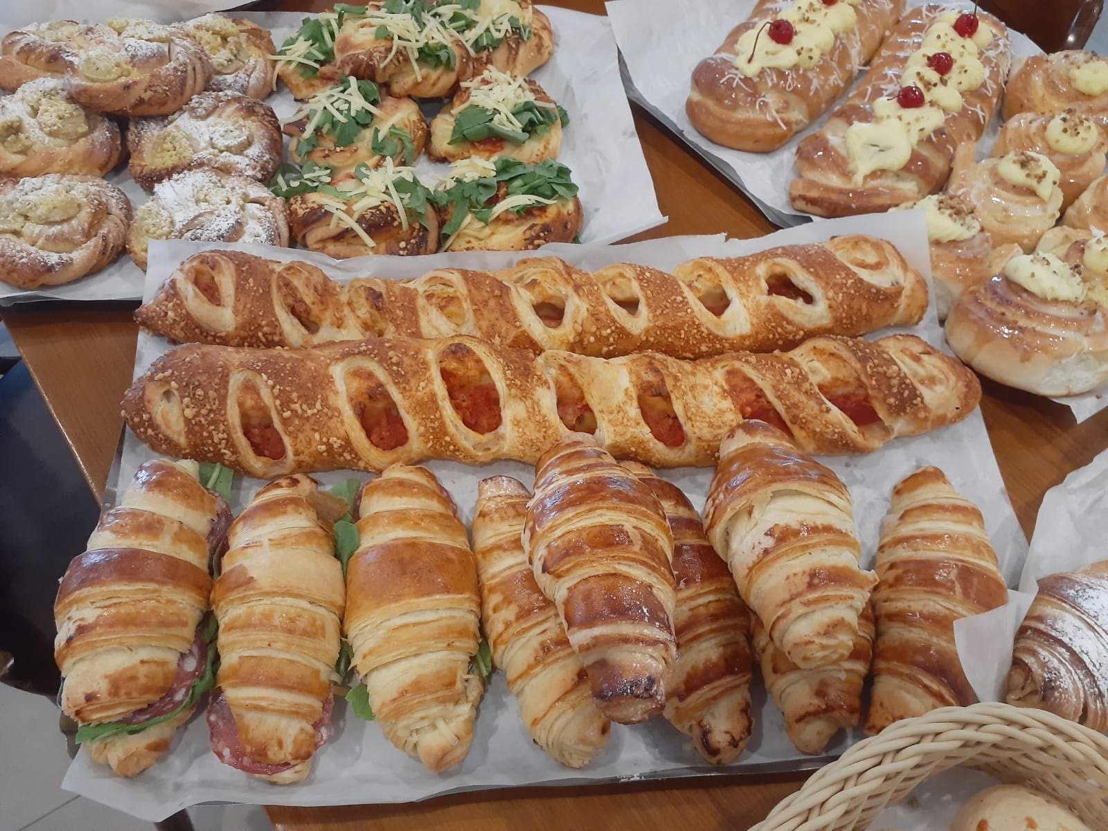 Diversos pães e croissants frescos em uma padaria, com detalhes de recheios e coberturas.