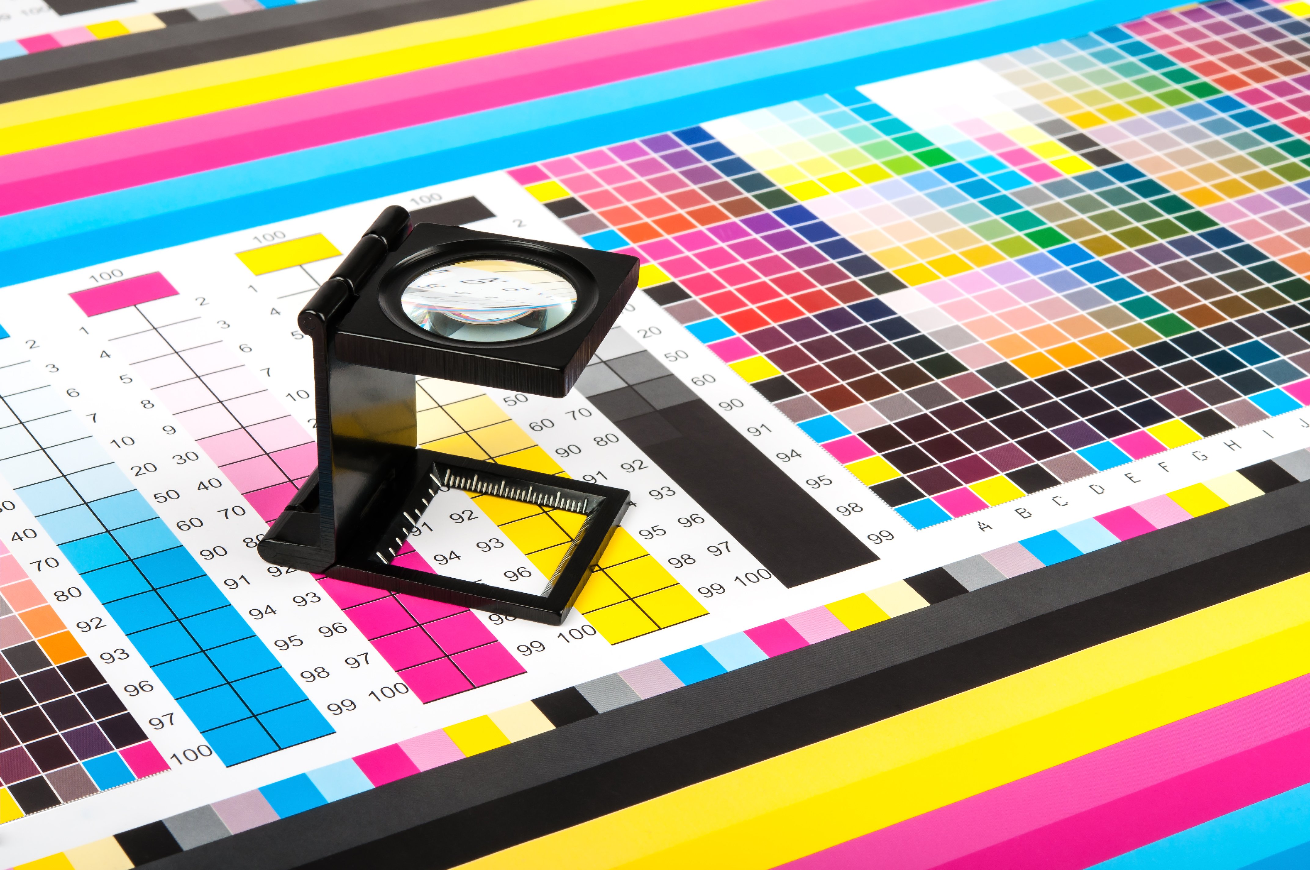 Magnifying glass on CMYK color calibration chart for print quality inspection