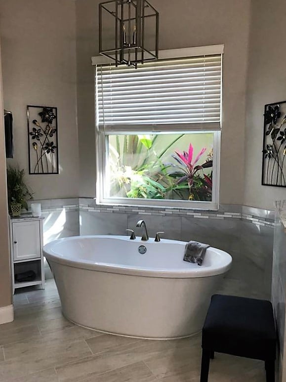Spa like oasis with free standing soaking tub featuring large grey tile and mosaic surround.  
