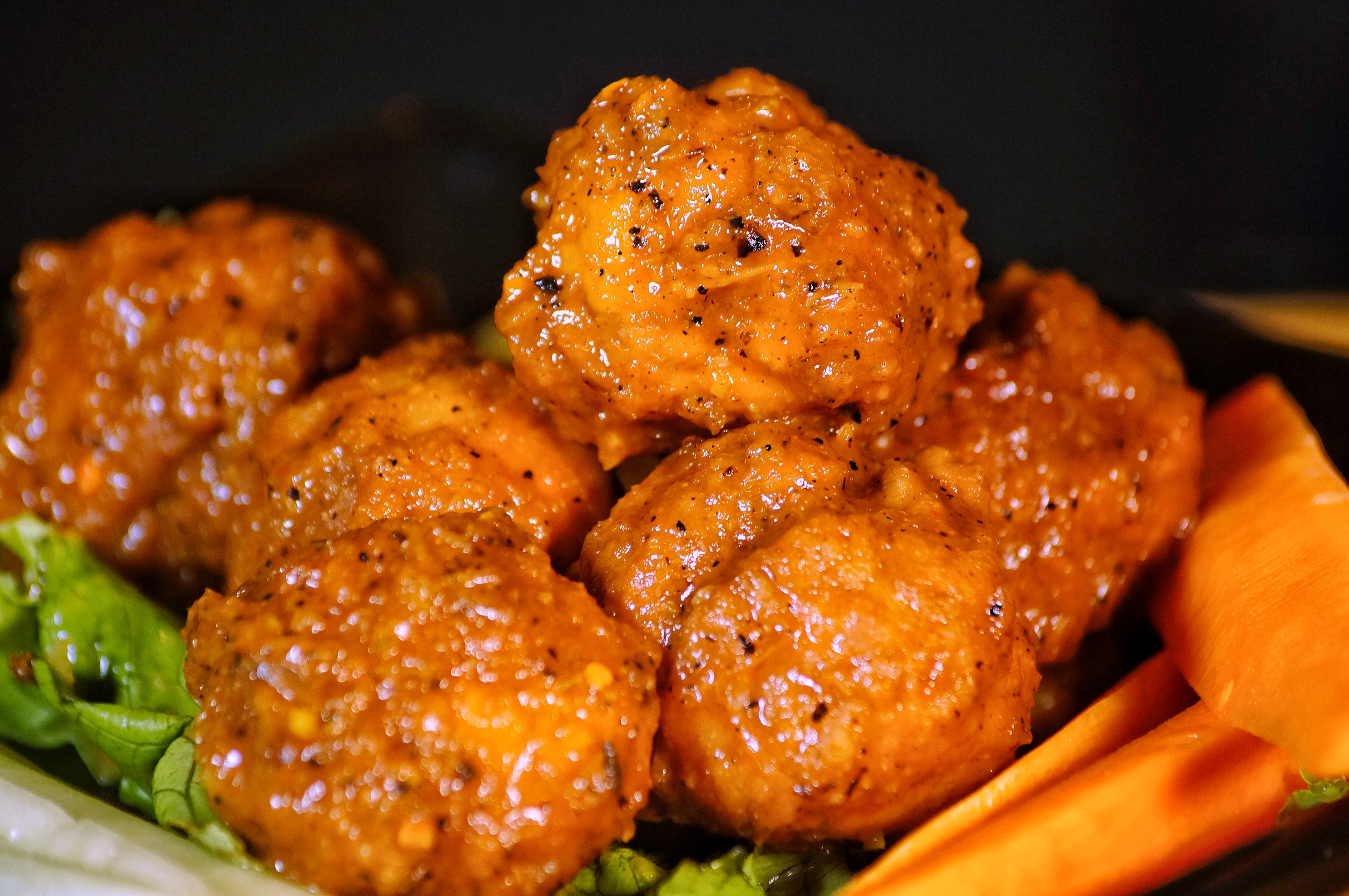 Close-up of spicy buffalo chicken wings with carrot sticks and lettuce on a dark plate