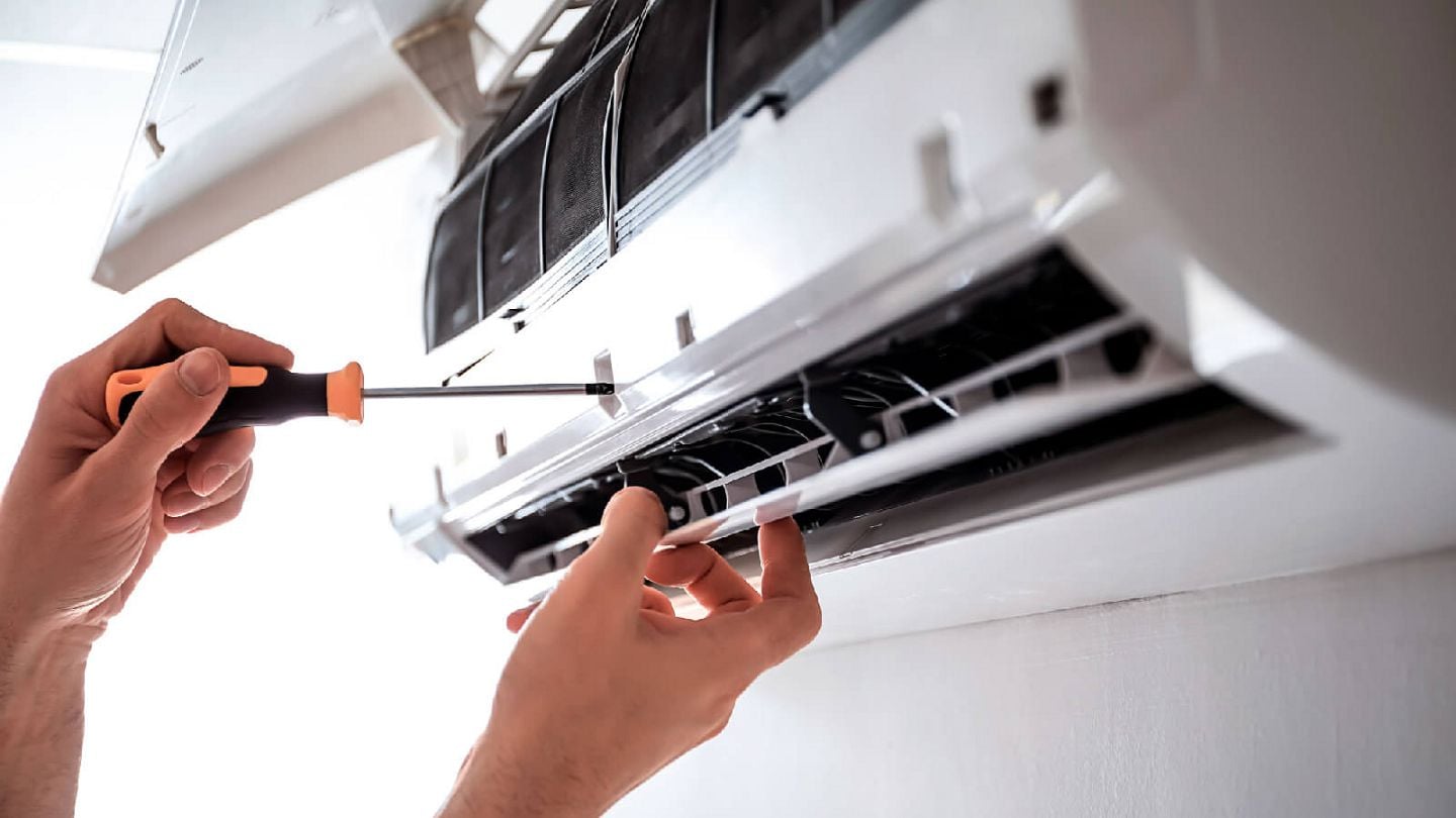Técnico reparando aire acondicionado split con destornillador durante mantenimiento del sistema de climatización